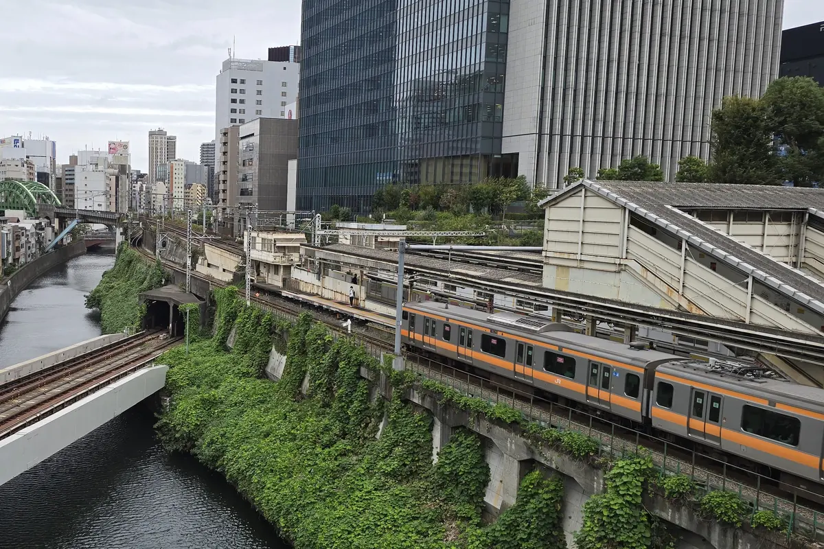 Un treno pendolare a strisce arancioni che corre lungo il fiume Kanda a Tokyo, con i grattacieli sullo sfondo
